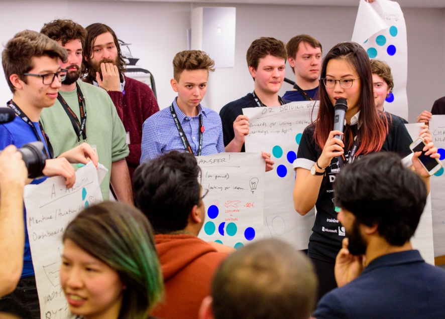 group of people holding flipchart pages around a woman with a microphone