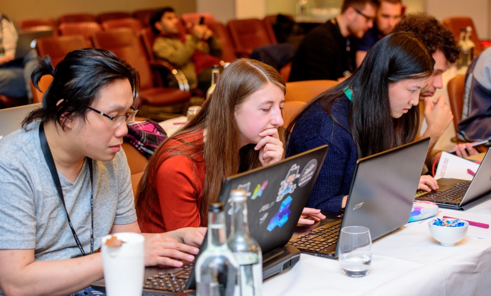 several people in a row seated at a table working at laptops