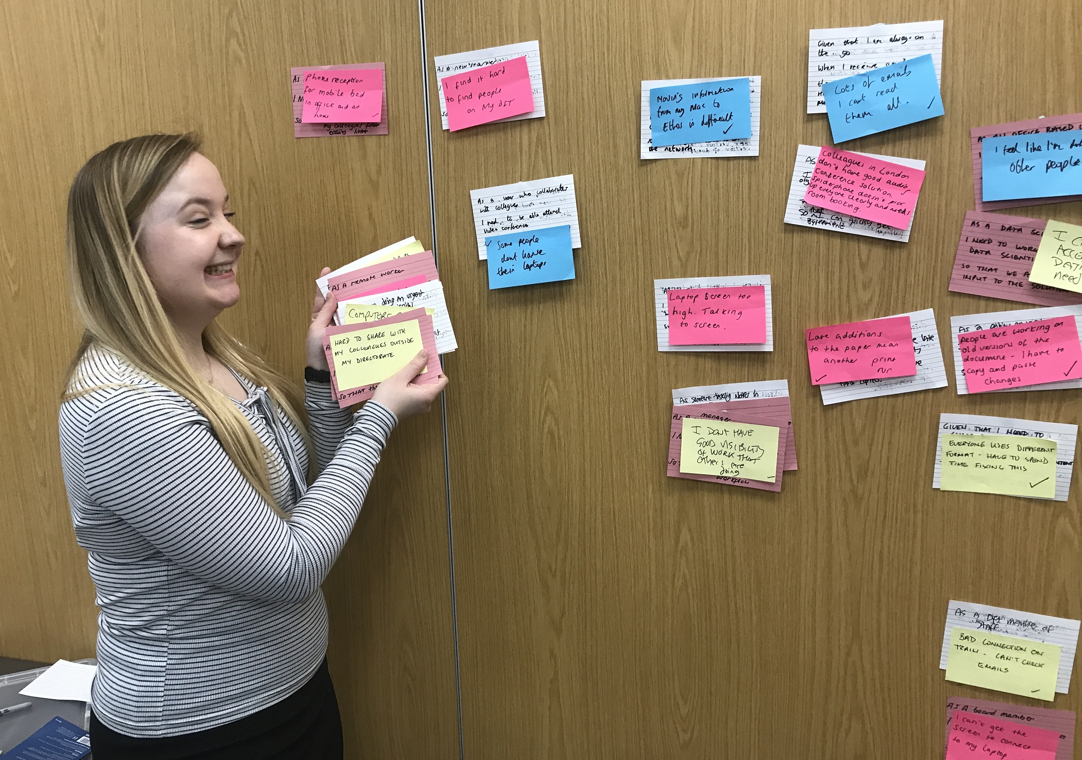 Gemma doing a card sort on a wooden wall using sticky notes