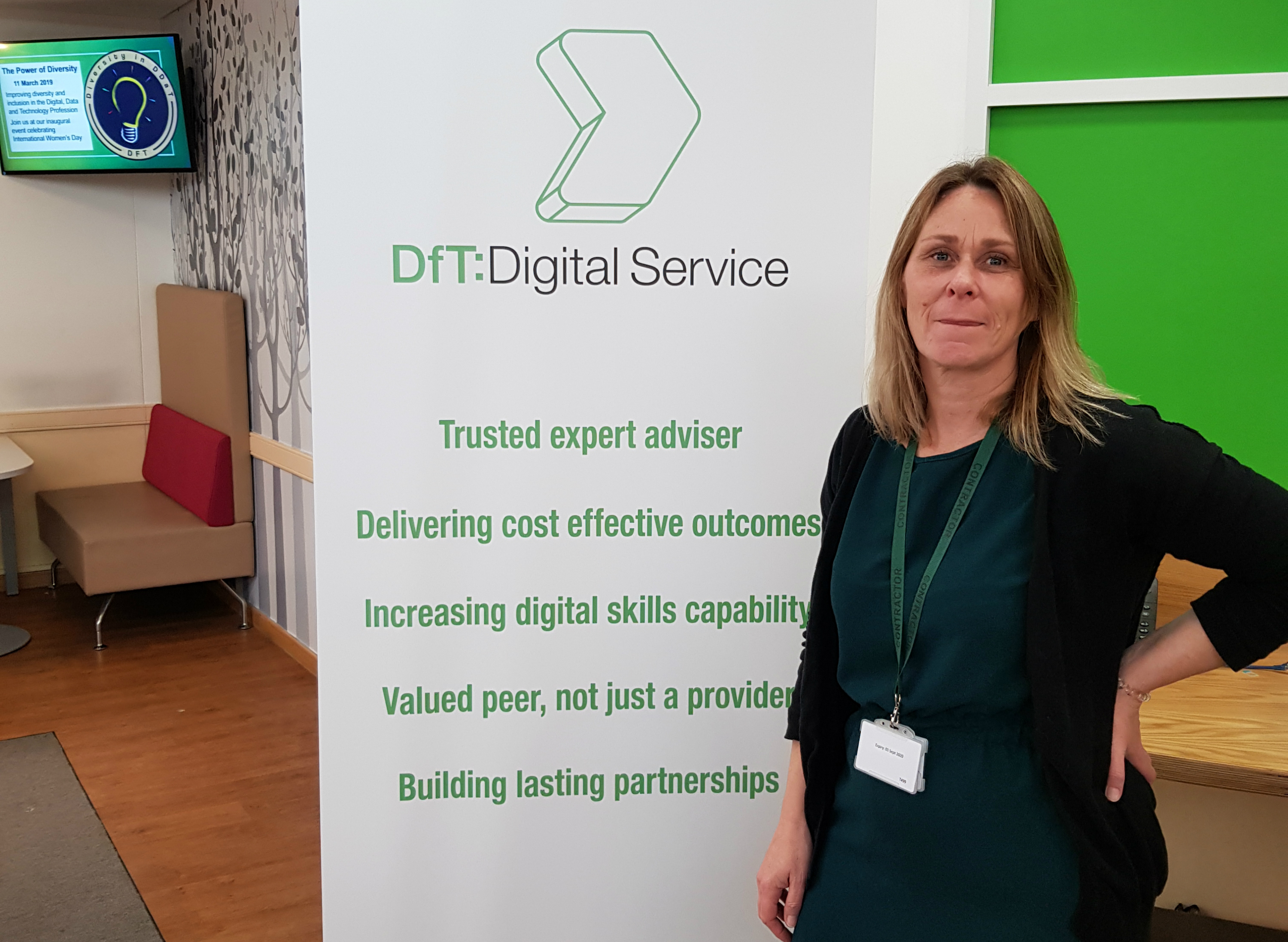Vanessa Hughes, alongside a banner that says DfT Digital Service. Trusted expert adviser. Delivering cost effective outcomes. Increasing digital skills capability. Valued peer, not just a provider. Building lasting partnerships. In the background, a video display advertises an International Women's Day event.